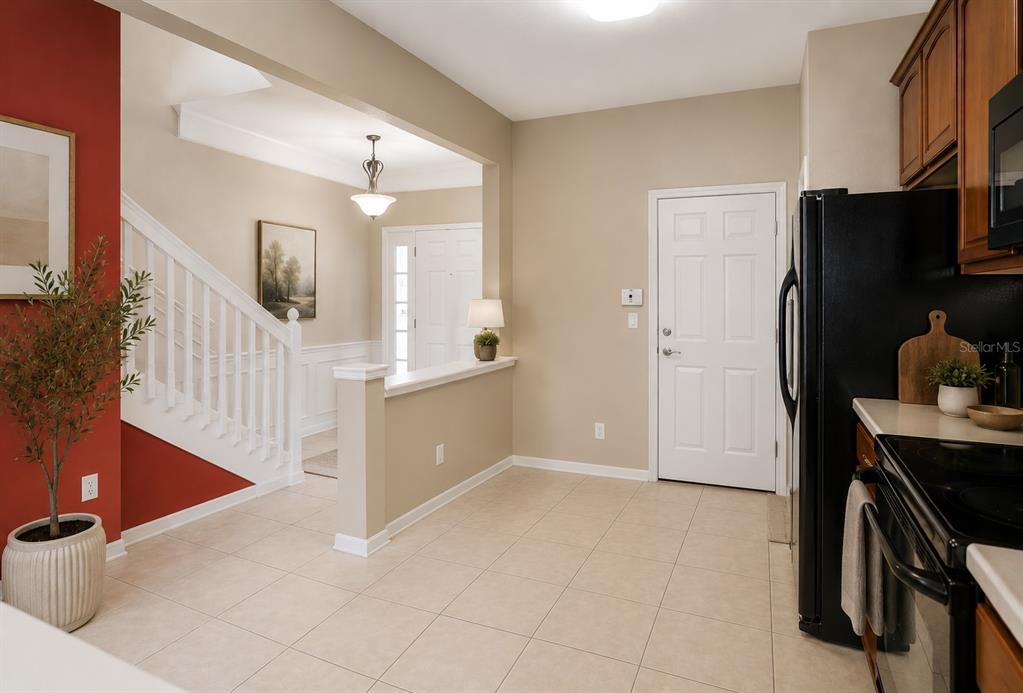 A kitchen with tile flooring opens to a foyer featuring a staircase and red wall — 6206 CASTELVEN DRIVE UNIT 104, ORLANDO, FL