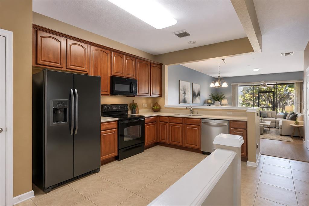 A kitchen with wood cabinets, black appliances, and tile flooring overlooks a living room area — 6206 CASTELVEN DRIVE UNIT 104, ORLANDO, FL