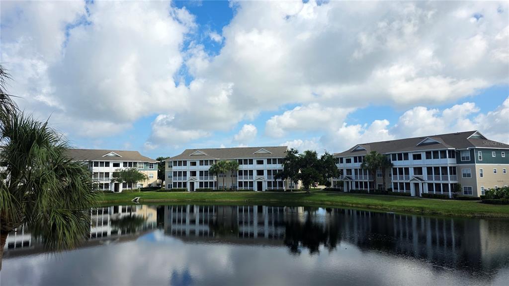Three multi-story apartment buildings stand behind a pond under a cloudy blue sky — 4802 51ST STREET W UNIT 1921, BRADENTON, FL