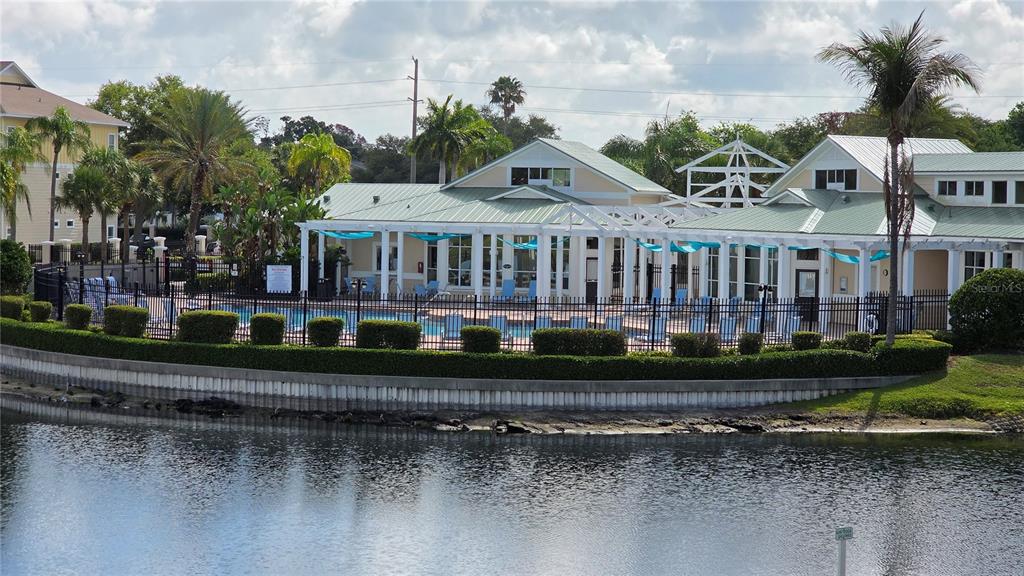 A swimming pool and clubhouse are situated behind a black fence next to a lake — 4802 51ST STREET W UNIT 1921, BRADENTON, FL