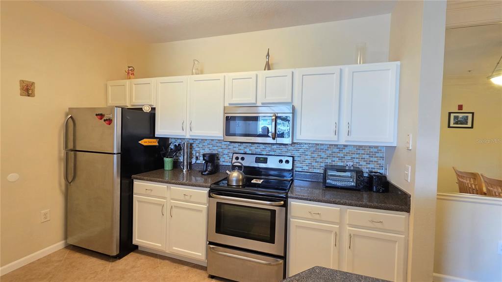 A kitchen features white cabinets, stainless steel appliances, and a blue tiled backsplash — 4802 51ST STREET W UNIT 1921, BRADENTON, FL