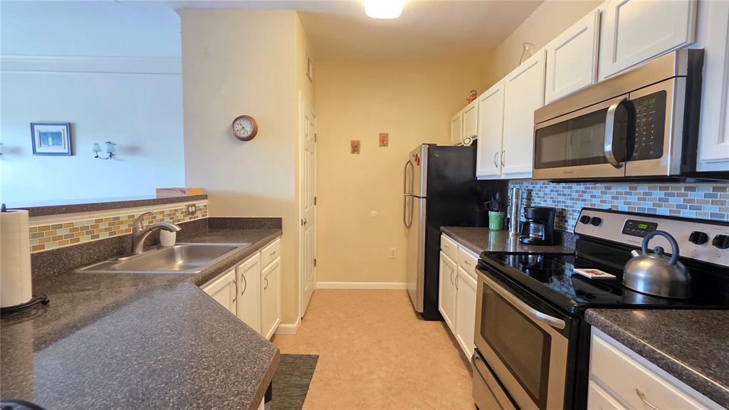 A kitchen features white cabinets, dark countertops, stainless steel appliances, and a tiled backsplash — 4802 51ST STREET W UNIT 1921, BRADENTON, FL