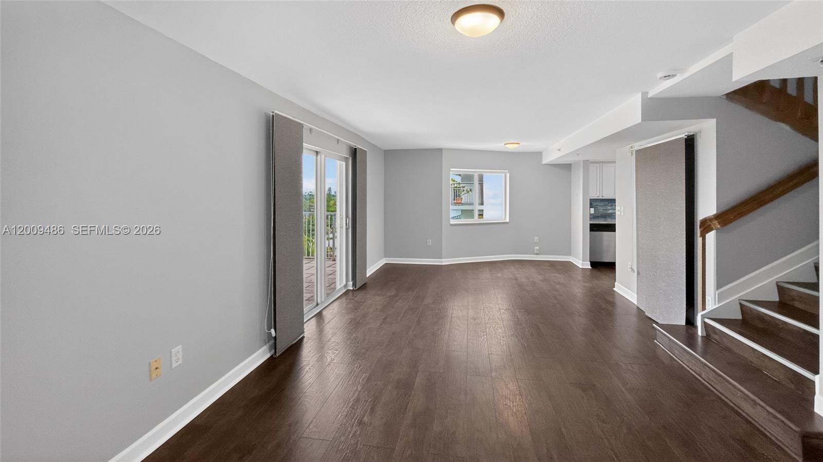 An empty room features dark wood flooring, light gray walls, a staircase, and sliding glass doors — 280 SW 20th Rd # 904, Miami FL 33129, MIAMI, FL