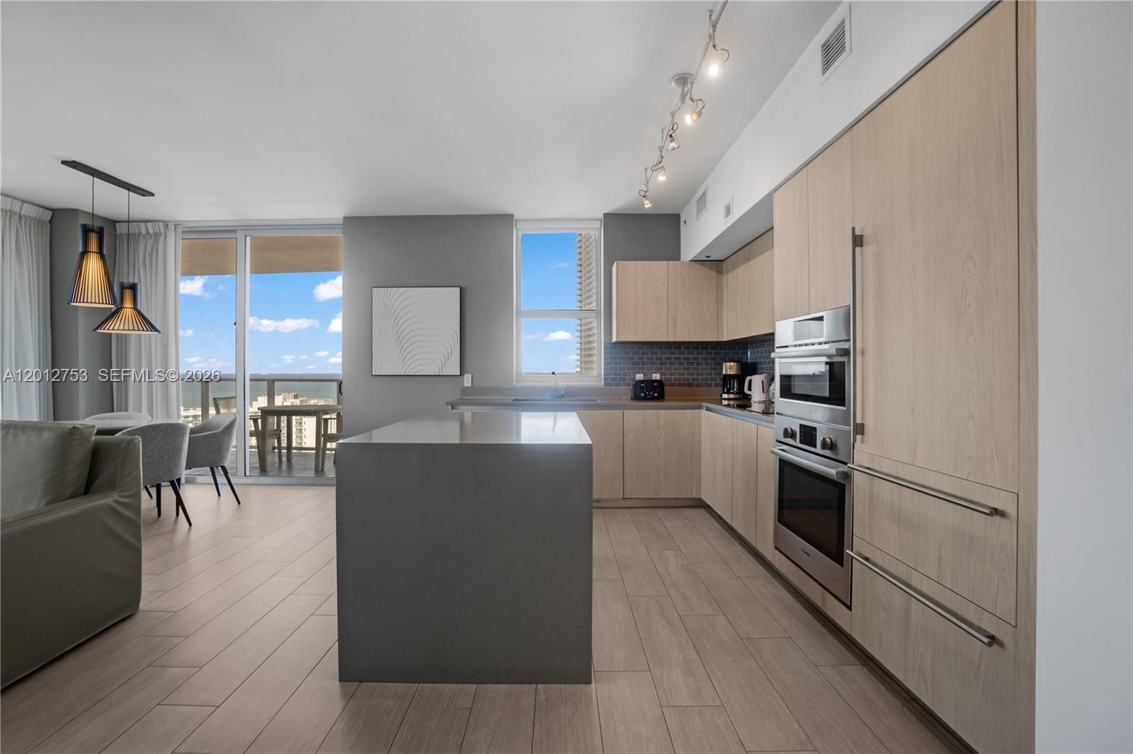 A modern kitchen features light wood cabinetry, a gray island, and a balcony with ocean views — 4010 S Ocean Dr # R1801, Hollywood FL 33019, HOLLYWOOD, FL