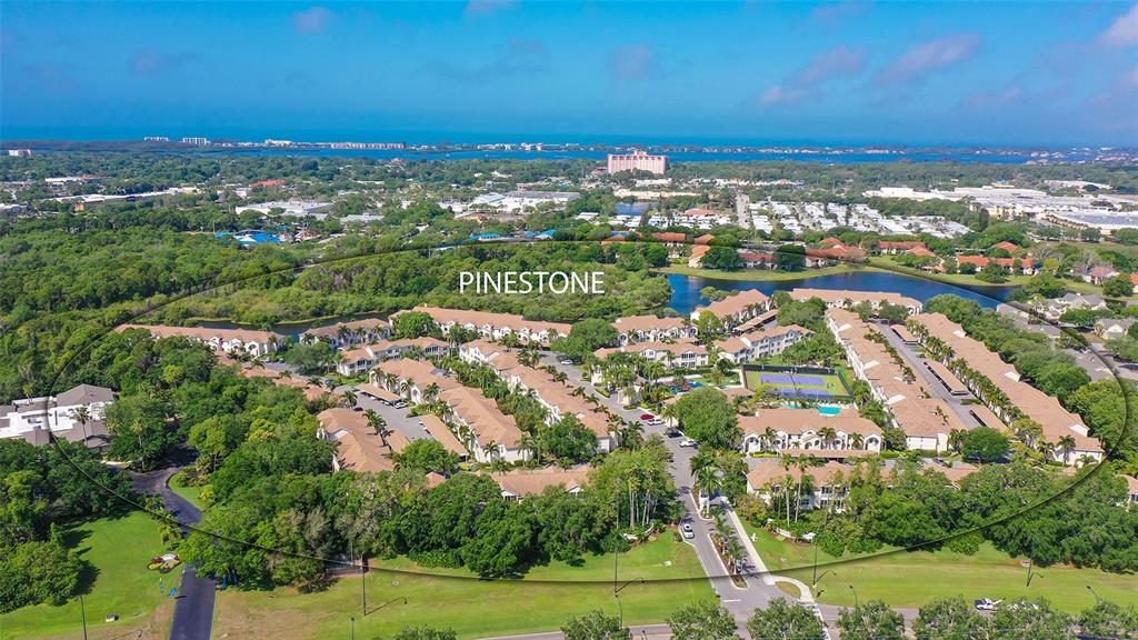 An aerial view shows the Pinestone residential community surrounded by lush trees and a lake — 4205 CASTLEBRIDGE LANE UNIT 1112, SARASOTA, FL