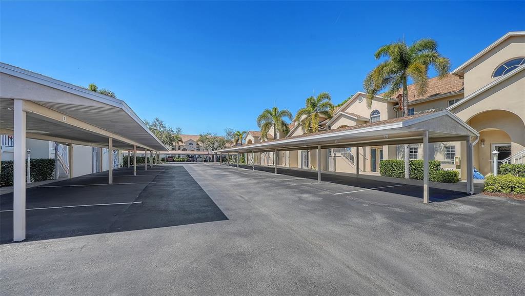 An outdoor parking lot with covered carports situated between two residential apartment buildings — 4205 CASTLEBRIDGE LANE UNIT 1112, SARASOTA, FL