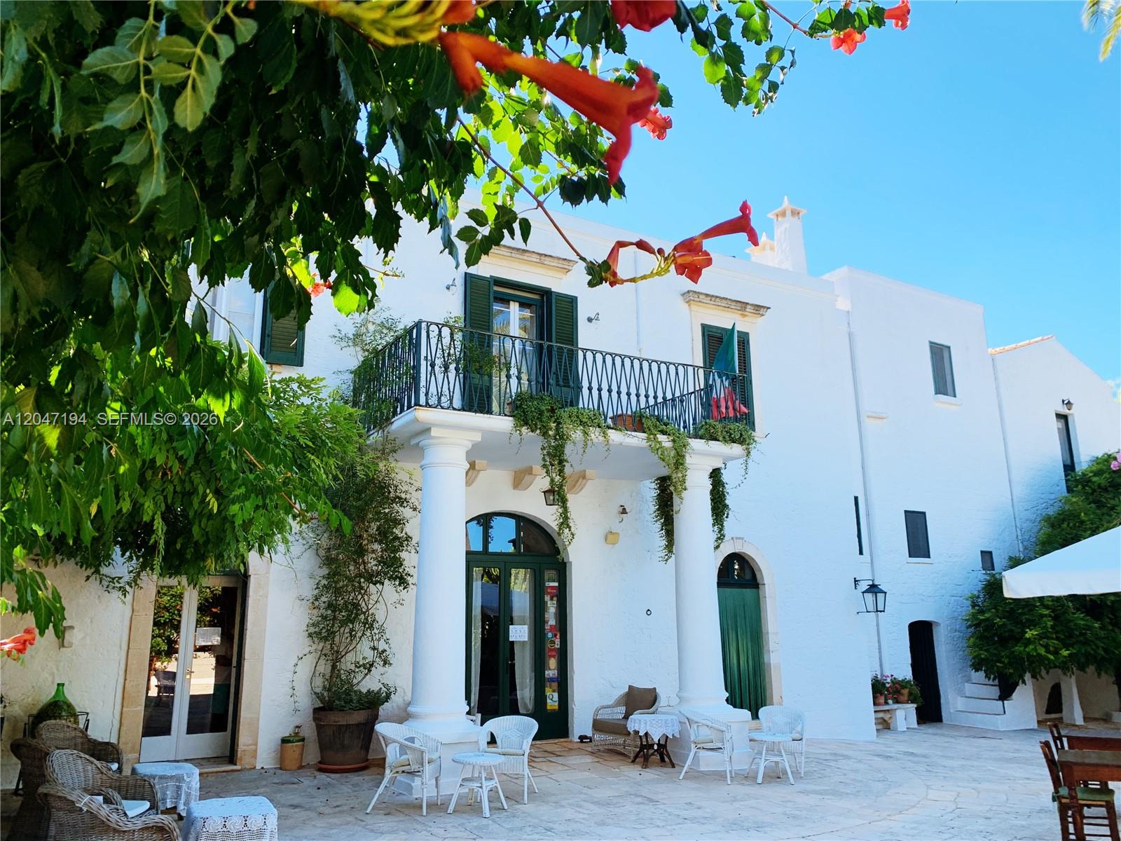 A white building with a balcony, columns, and a patio area with outdoor furniture — AR