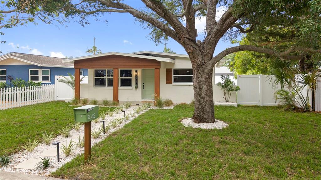 A single-story house with a white exterior, wood-trimmed porch, and a large tree in front — 7042 DARTMOUTH AVENUE N, ST PETERSBURG, FL
