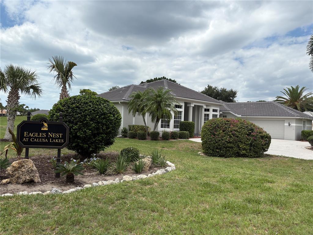 A single-story house with a gray tile roof and a community sign in the foreground — 2181 CALUSA LAKES BOULEVARD, NOKOMIS, FL