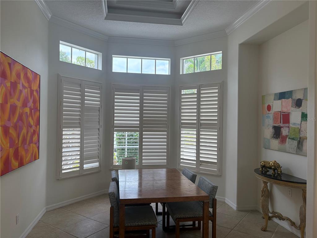 A dining area features a bay window with plantation shutters, tile floors, and wall art — 2181 CALUSA LAKES BOULEVARD, NOKOMIS, FL