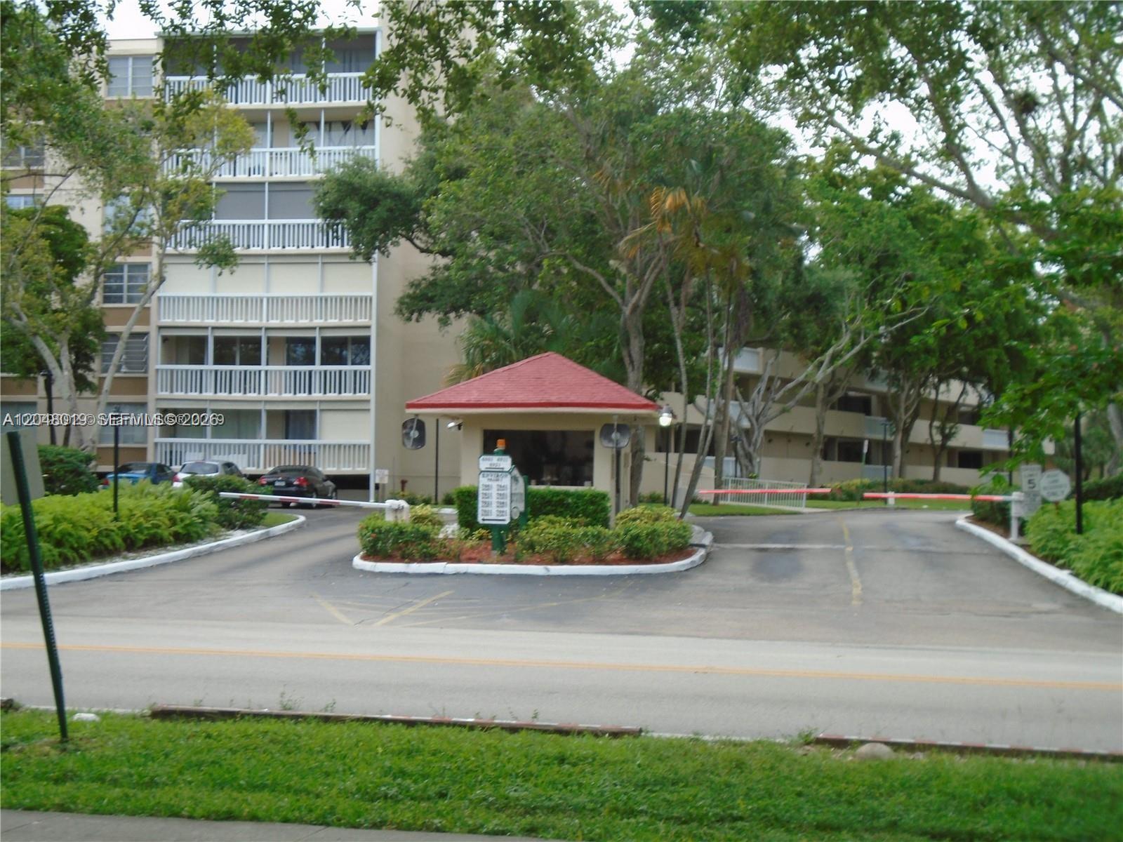 A gated entrance with a guardhouse and a multi-story residential building in the background — 6921 Environ Blvd # 4P, Lauderhill FL 33319, LAUDERHILL, FL