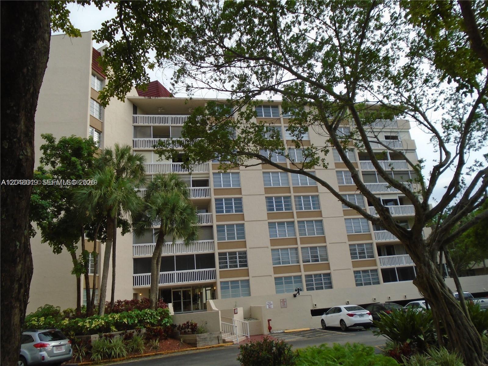 A multi-story apartment building features screened balconies, tan exterior walls, and a parking lot — 6921 Environ Blvd # 4P, Lauderhill FL 33319, LAUDERHILL, FL