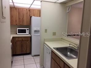A kitchen with wood cabinets, white appliances, a stainless steel sink, and tiled flooring — 120 HIBISCUS WOODS COURT UNIT 10B, DELTONA, FL