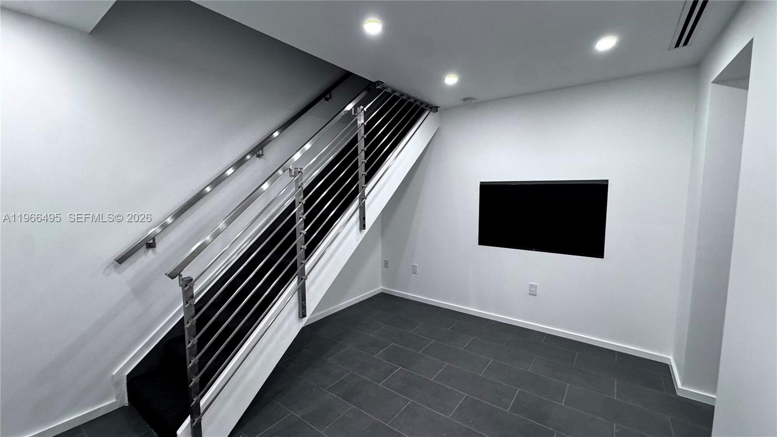 A modern entryway features dark tile flooring, white walls, and a metal-railed staircase — 13406 SW 128th St, Miami FL 33186, MIAMI, FL