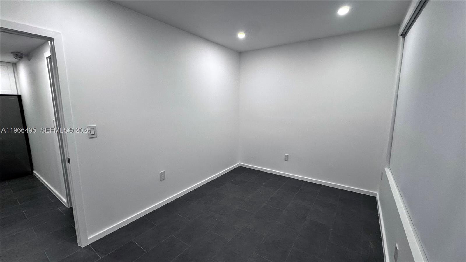 A minimalist room features white walls, dark tile flooring, a window, and an open door — 13406 SW 128th St, Miami FL 33186, MIAMI, FL