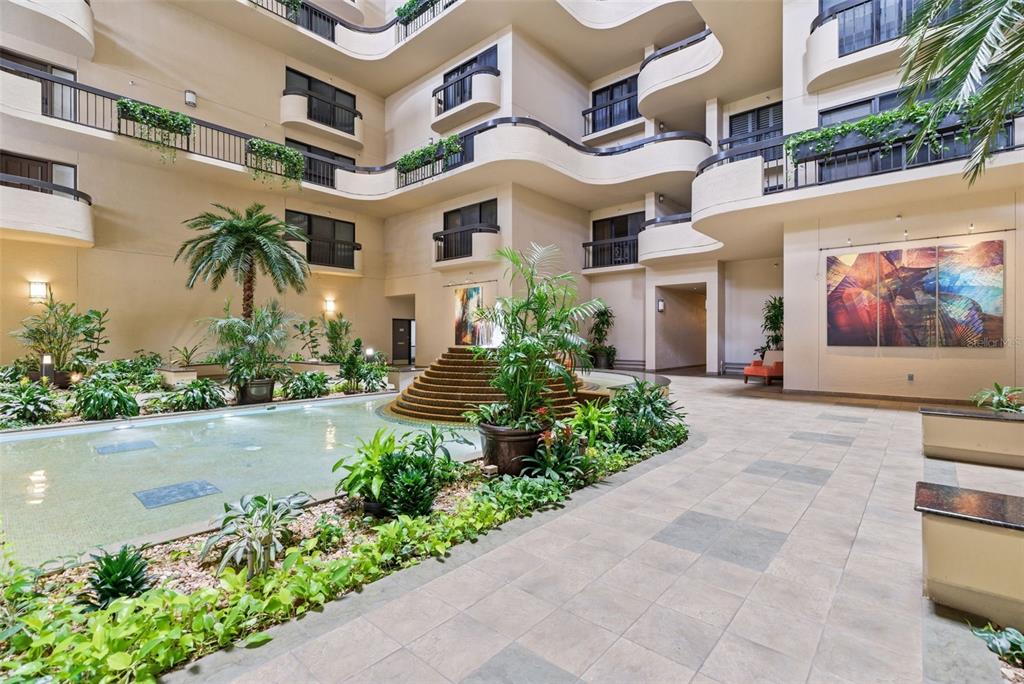 An indoor atrium features a tiered fountain, lush tropical plants, and multi-level balconies — 2413 BAYSHORE BOULEVARD UNIT 1004, TAMPA, FL