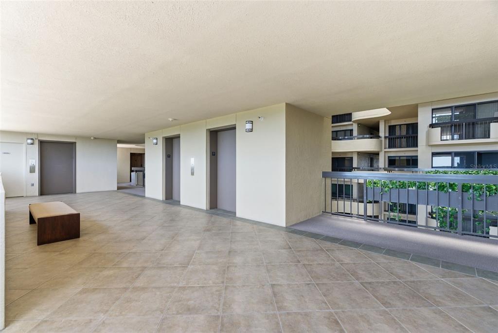 An open-air apartment building hallway features tiled flooring, two elevators, and a metal railing — 2413 BAYSHORE BOULEVARD UNIT 1004, TAMPA, FL