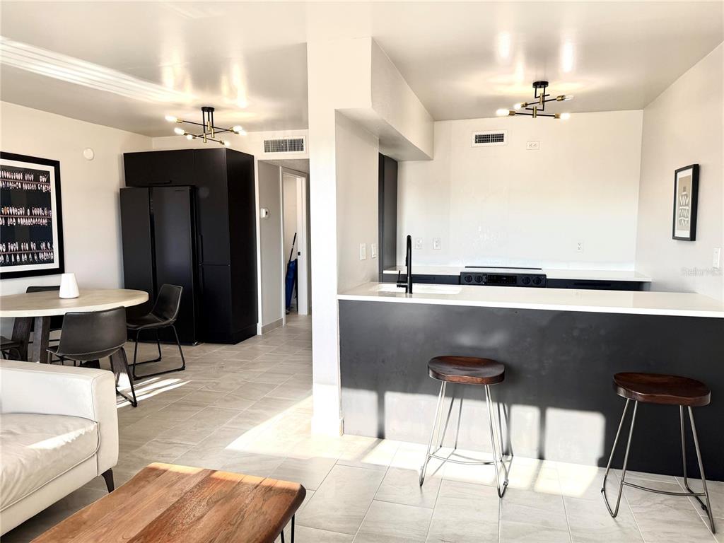 A modern kitchen features black cabinetry, white countertops, and a breakfast bar with two stools — 2525 W BAY DRIVE UNIT C34, LARGO, FL