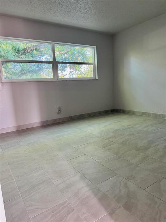 An empty room with light-colored tile flooring and a large window overlooking trees — 2525 W BAY DRIVE UNIT C34, LARGO, FL