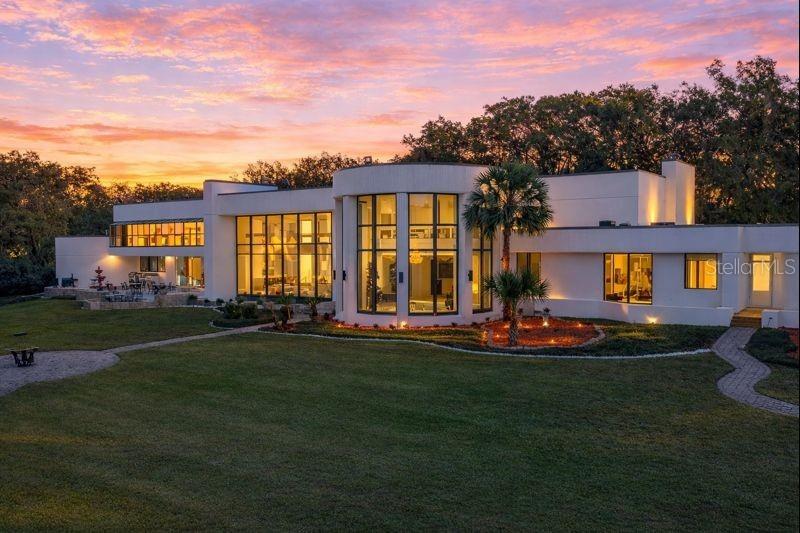 A modern white house with large windows and a curved facade sits on a grassy lawn — 812 SWEETWATER CLUB BOULEVARD, LONGWOOD, FL