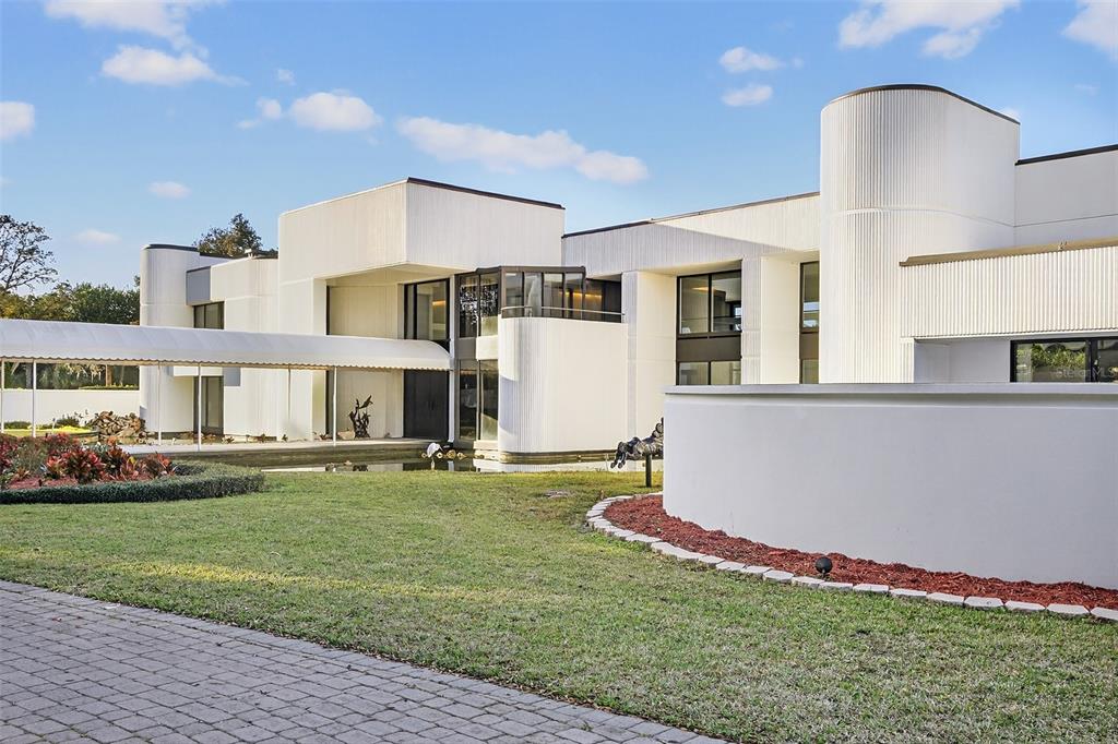 A modern white building with a curved facade, a covered walkway, and a front pond — 812 SWEETWATER CLUB BOULEVARD, LONGWOOD, FL