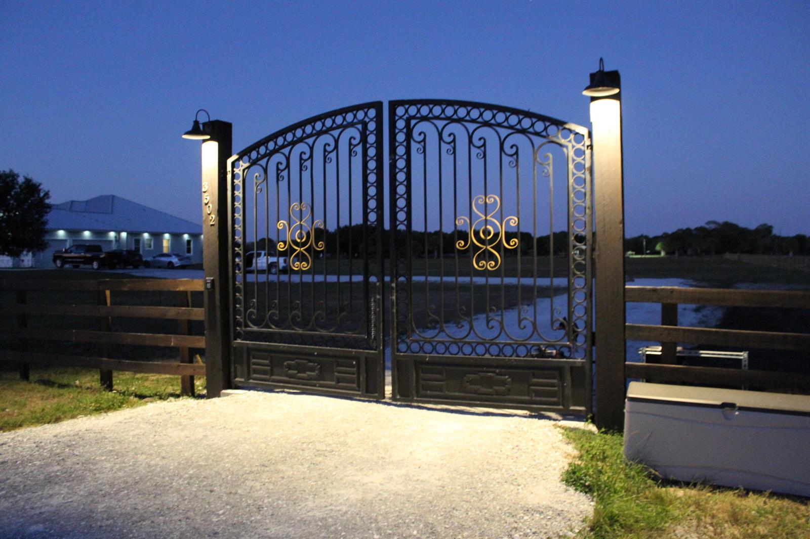 A black metal gate with gold accents stands at the entrance of a gravel driveway — 3502 S Brocksmith Road, Fort Pierce FL 34945, FORT PIERCE, FL