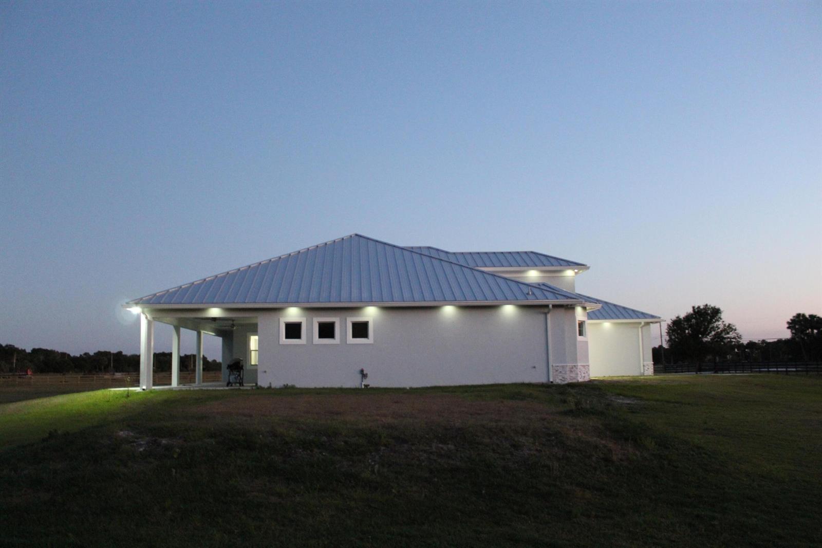 A side view of a modern house with a metal roof and exterior wall lighting — 3502 S Brocksmith Road, Fort Pierce FL 34945, FORT PIERCE, FL