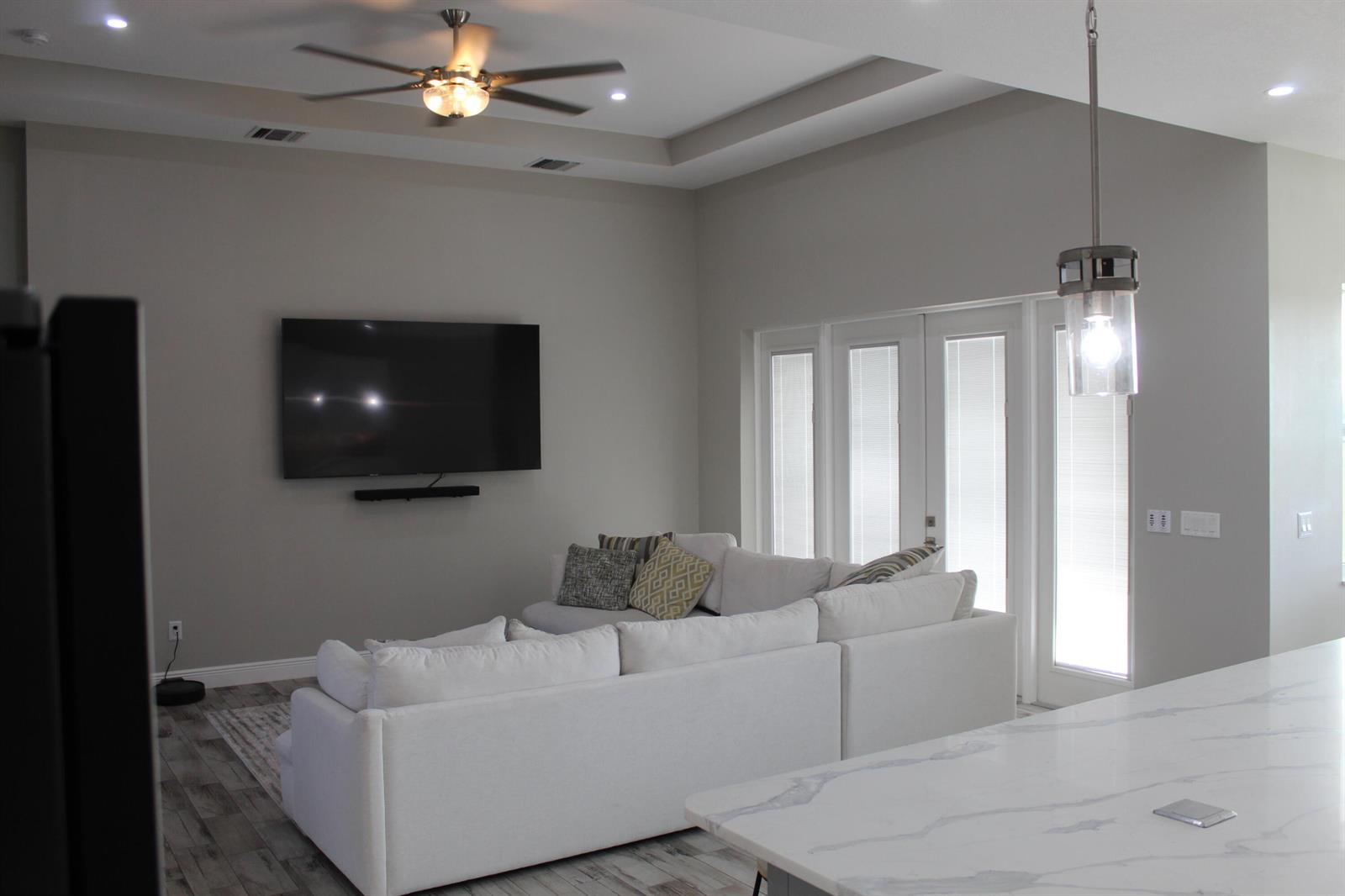 A living room with a white sectional sofa, wall-mounted television, and tray ceiling — 3502 S Brocksmith Road, Fort Pierce FL 34945, FORT PIERCE, FL