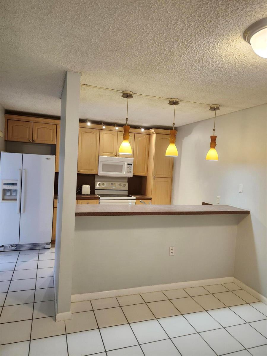 A kitchen with light wood cabinets, white appliances, and a breakfast bar with pendant lighting — 3209 32nd Way, West Palm Beach FL 33407, WEST PALM BEACH, FL