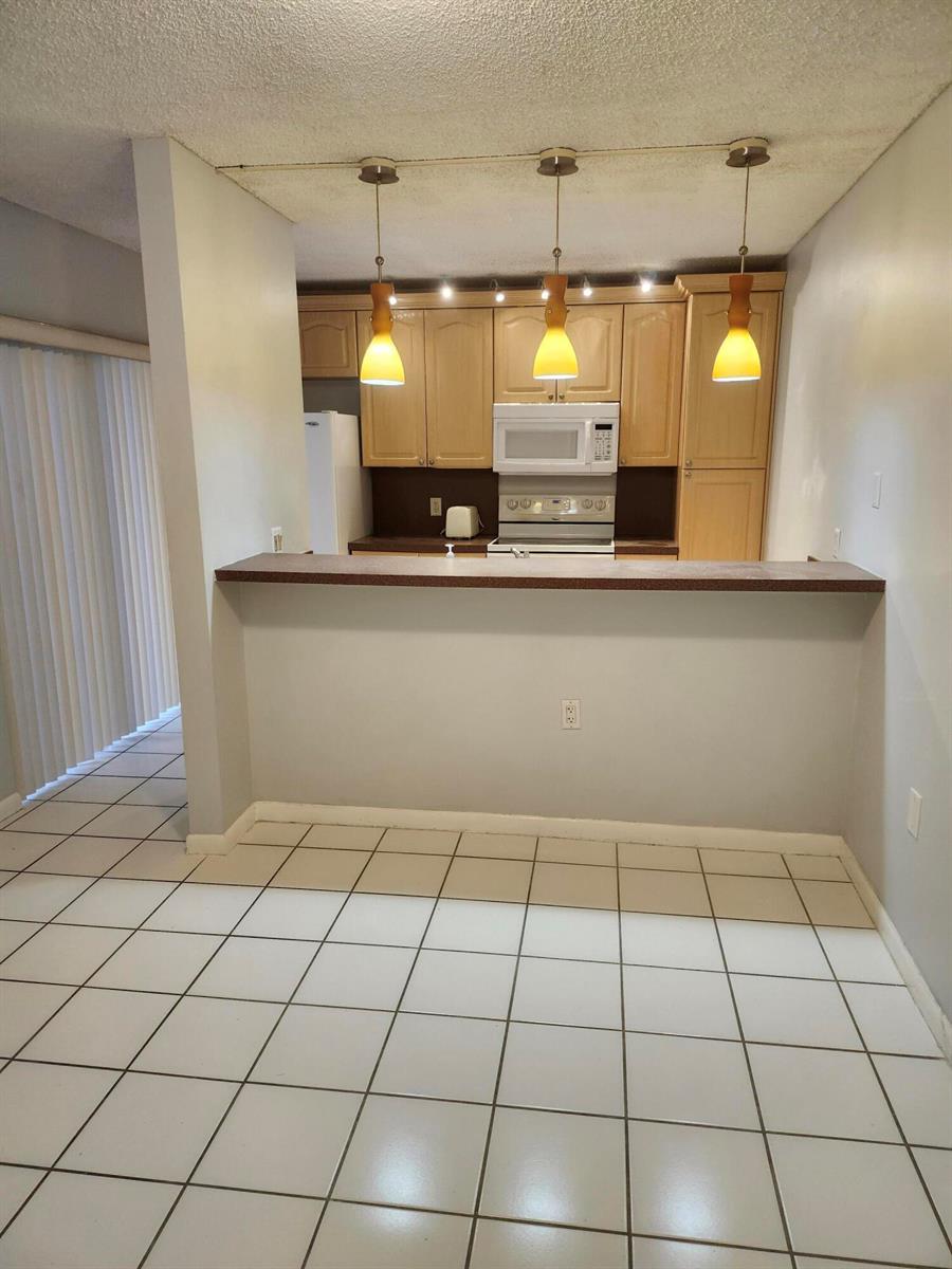 A kitchen with light wood cabinets, a breakfast bar, and white tile flooring — 3209 32nd Way, West Palm Beach FL 33407, WEST PALM BEACH, FL