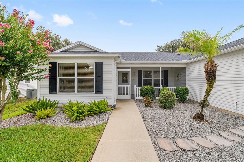 A white house with black shutters, a concrete walkway, and a landscaped front yard — 187 OLANTA DRIVE, THE VILLAGES, FL