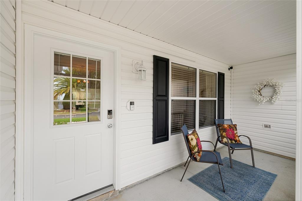 A white front door and two chairs sit on a covered porch with white siding — 187 OLANTA DRIVE, THE VILLAGES, FL