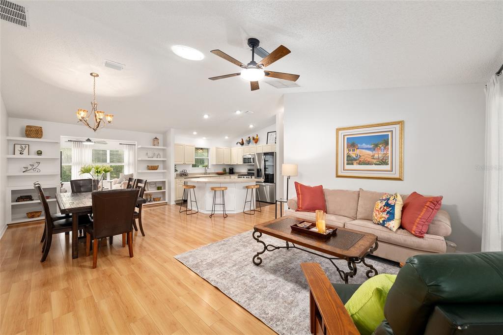 An open-concept living and dining area features light wood flooring, a kitchen island, and furniture — 187 OLANTA DRIVE, THE VILLAGES, FL