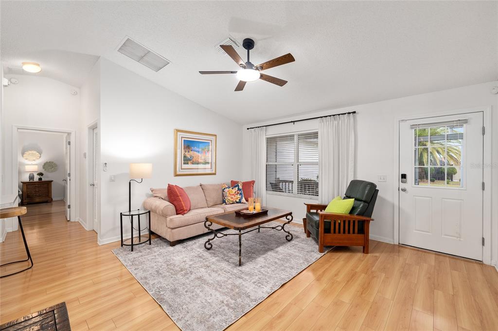 A living room features light wood flooring, a beige sofa, a dark armchair, and a ceiling fan — 187 OLANTA DRIVE, THE VILLAGES, FL