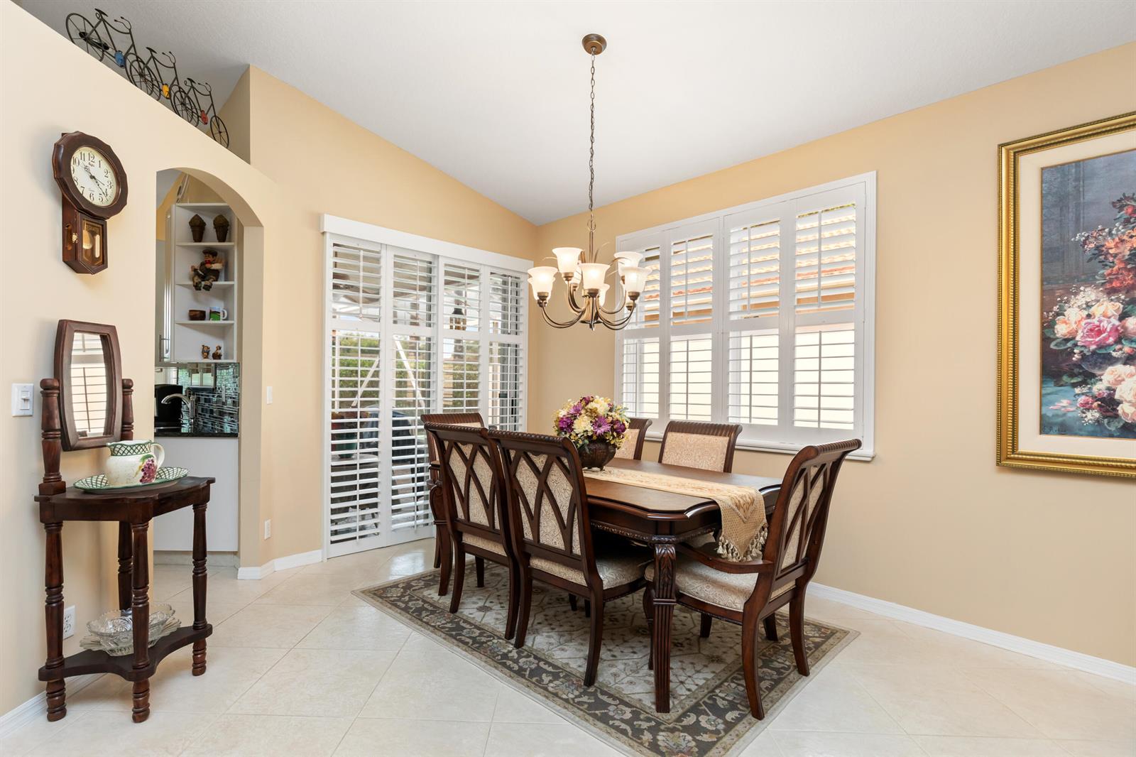A dining room features a wooden table, six chairs, a chandelier, and plantation shutters — 6698 Vía Roma, Delray Beach FL 33446, DELRAY BEACH, FL