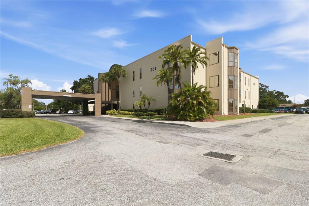 A three-story tan building with a covered entrance and palm trees under a blue sky — 201 HILDA STREET UNIT 22, KISSIMMEE, FL