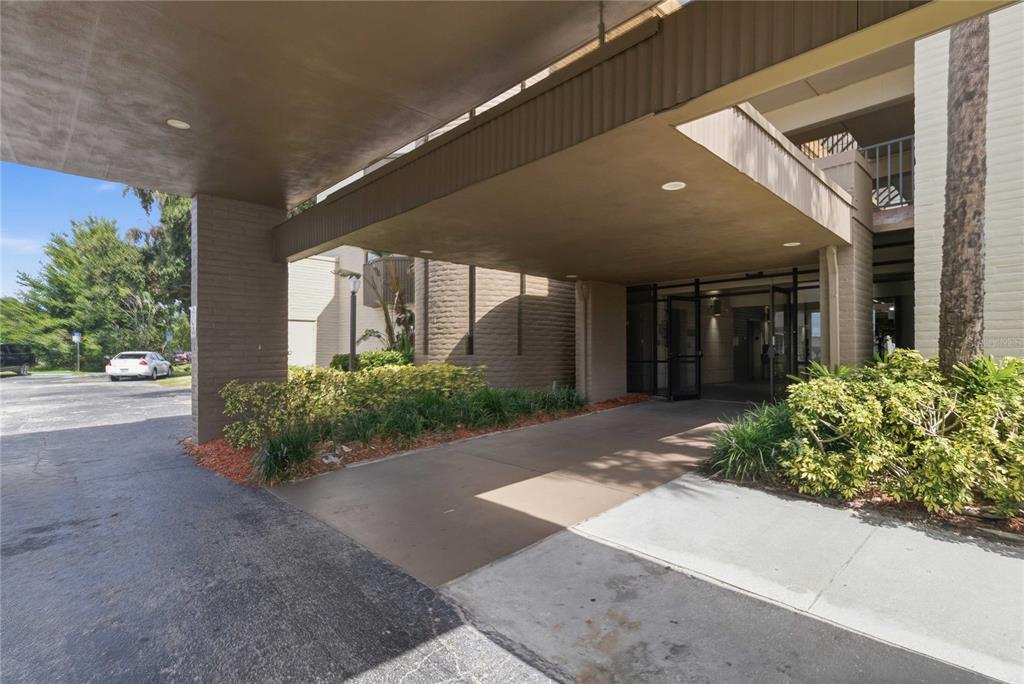 A covered porte-cochere leads to the glass-paned entrance of a multi-story apartment building — 201 HILDA STREET UNIT 22, KISSIMMEE, FL