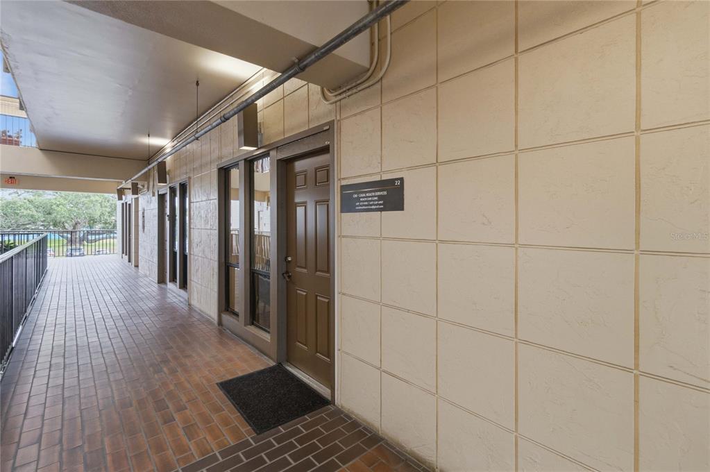 An exterior walkway with brick flooring leads to a brown door labeled number 22 — 201 HILDA STREET UNIT 22, KISSIMMEE, FL