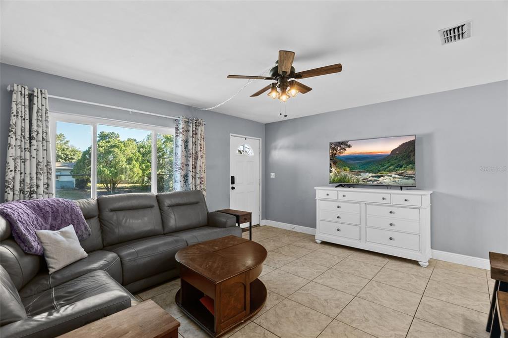 A living room features a grey sofa, a white dresser with a television, and tile flooring — 4817 DRIFT TIDE DRIVE, NEW PORT RICHEY, FL