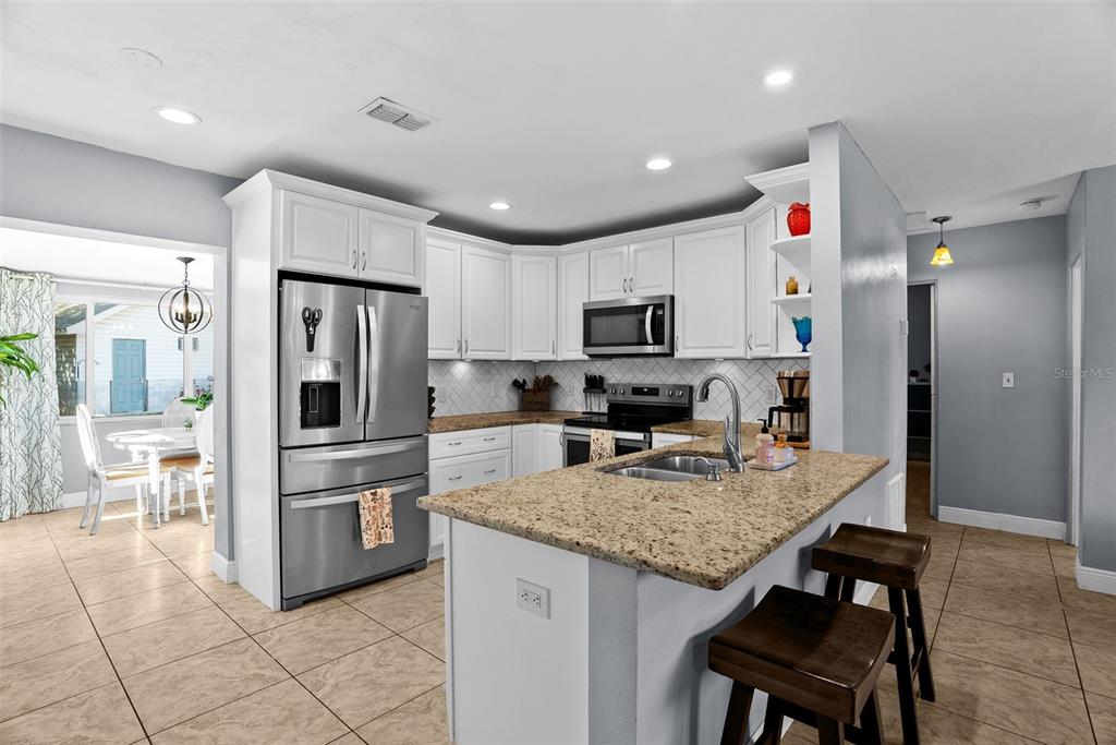 A kitchen features white cabinetry, granite countertops, a stainless steel refrigerator, and a breakfast island — 4817 DRIFT TIDE DRIVE, NEW PORT RICHEY, FL