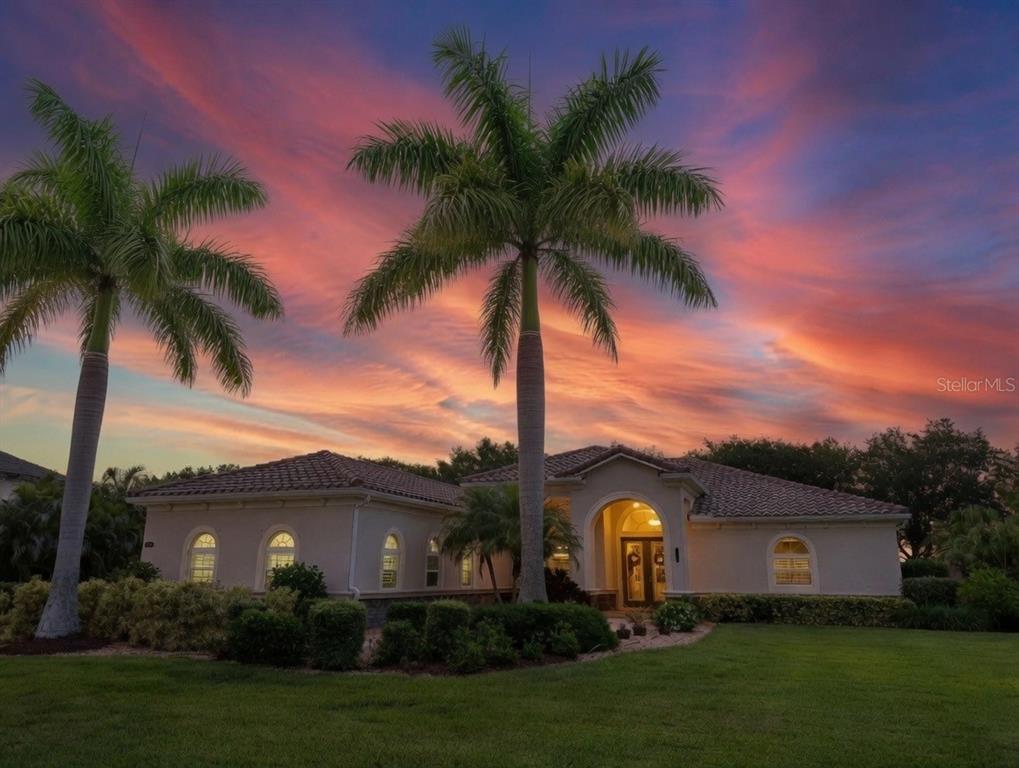 A single-story stucco house with a tiled roof stands under a vibrant sunset sky — 380 165TH COURT NE, BRADENTON, FL