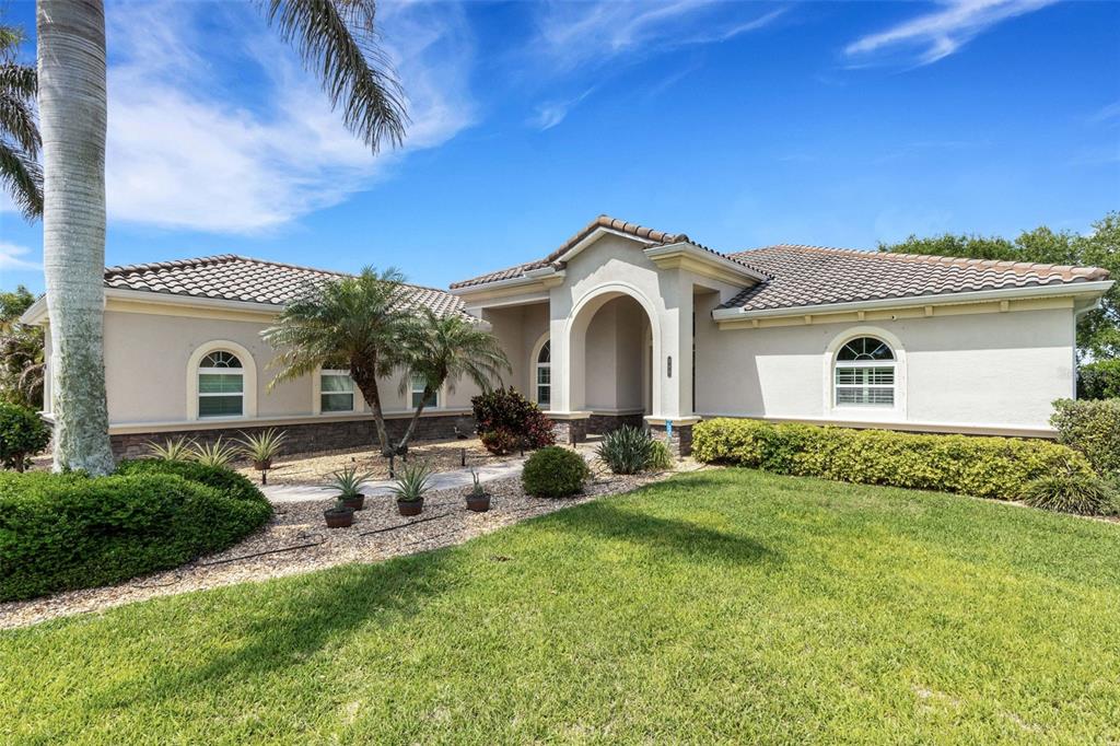 A single-story stucco house with a tiled roof, arched entryway, and landscaped front yard — 380 165TH COURT NE, BRADENTON, FL