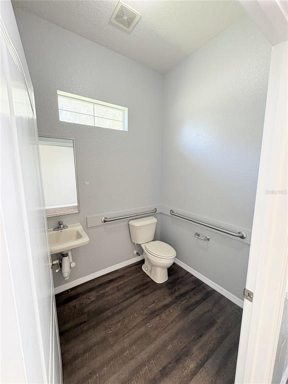 A small, accessible bathroom with a toilet, wall-mounted sink, grab bars, and dark wood flooring — 1701 NE 42ND AVENUE UNIT 403, OCALA, FL