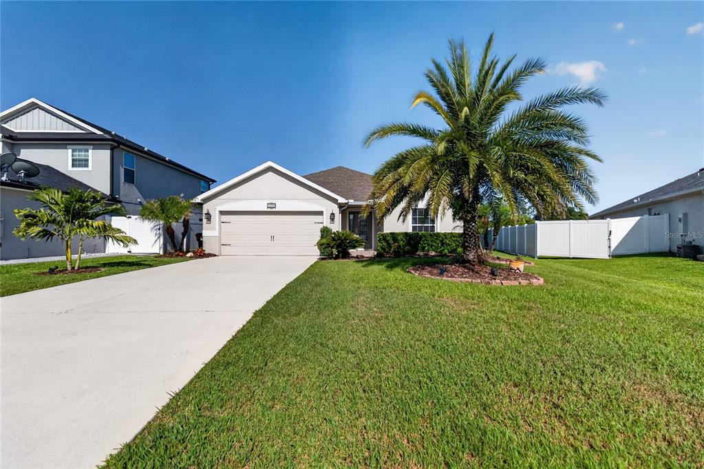A single-story house with a two-car garage, a palm tree, and a white vinyl fence — 3438 BARINA STREET, ST CLOUD, FL