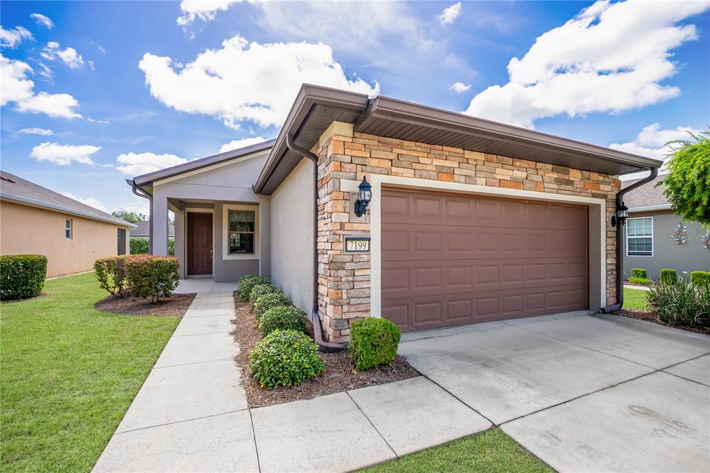 A single-story house with a stone-accented garage, brown door, and a concrete driveway — 7199 SW 91ST COURT, OCALA, FL