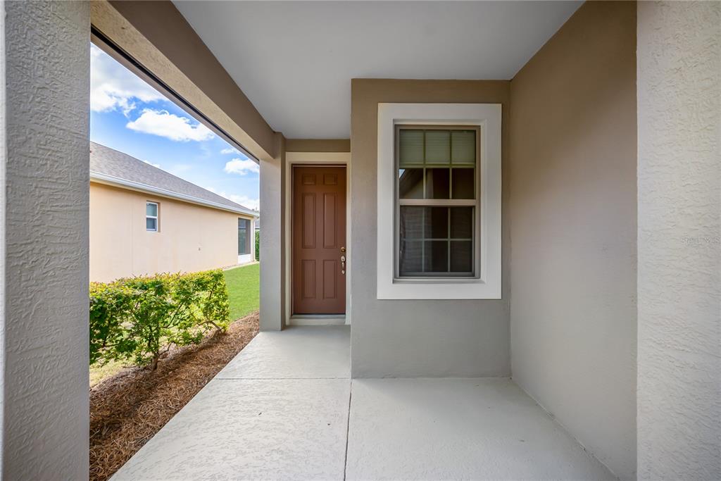 A covered concrete entryway features a brown front door and a single window — 7199 SW 91ST COURT, OCALA, FL