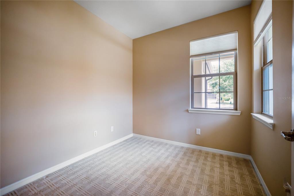 An empty room features tan walls, patterned carpet, and two windows with blinds — 7199 SW 91ST COURT, OCALA, FL