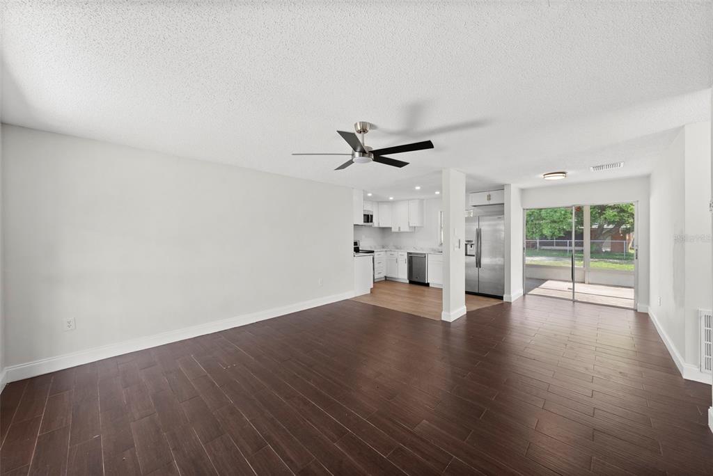 An open-concept living area with dark wood floors, a ceiling fan, and an adjacent kitchen — 7645 ARLIGHT DRIVE, NEW PORT RICHEY, FL