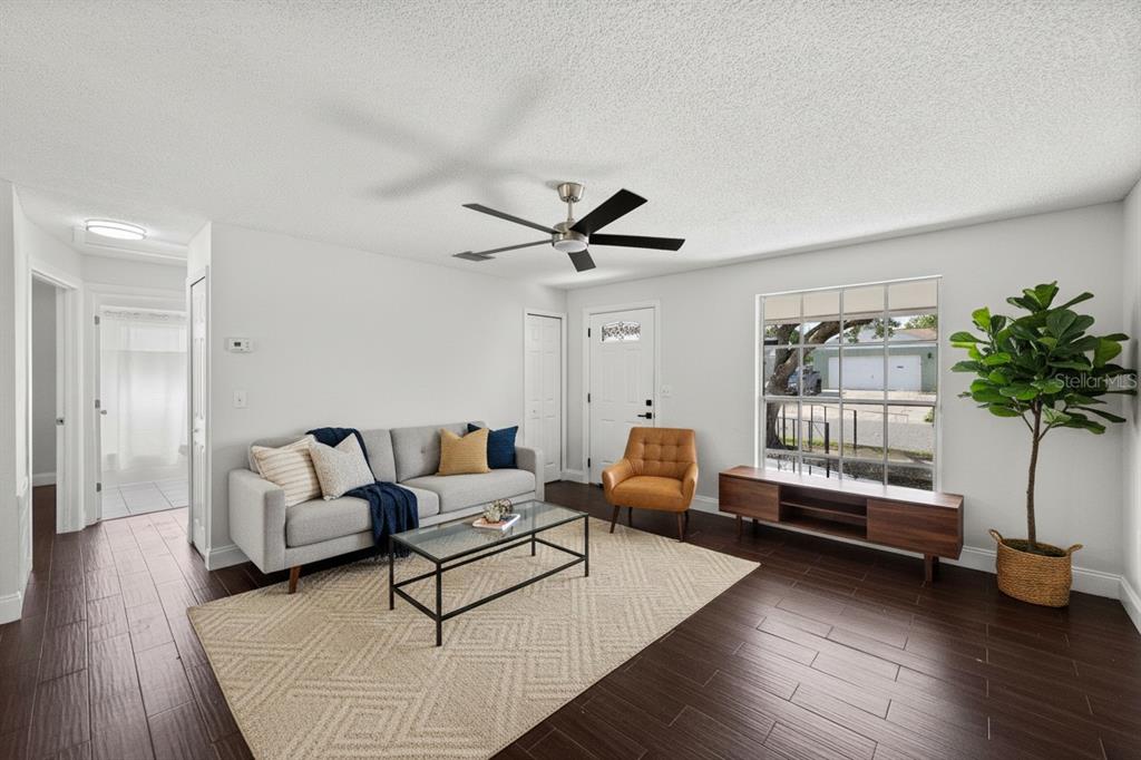 A living room features a gray sofa, a glass coffee table, and dark wood flooring — 7645 ARLIGHT DRIVE, NEW PORT RICHEY, FL
