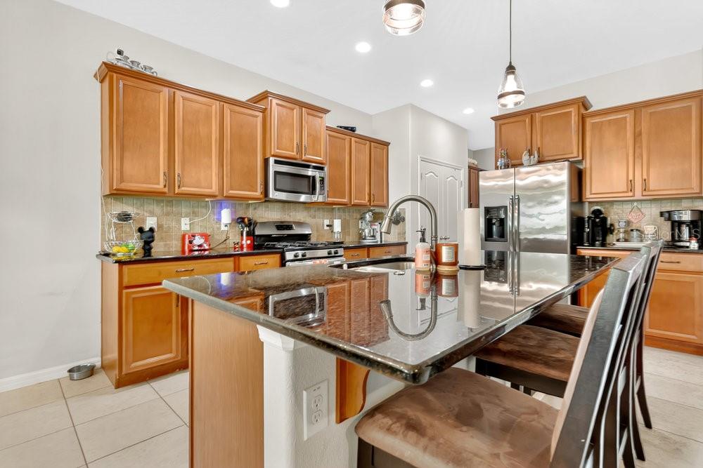 A kitchen features wood cabinets, granite countertops, a stainless steel refrigerator, and a center island — 632 MEADOW SAGE DRIVE, DELAND, FL